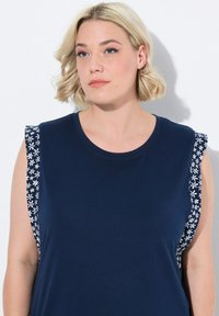Marineblauw tanktop met bloemenpatronen op de schouders, met een ronde halslijn en korte mouwen. Gemaakt van zacht materiaal.