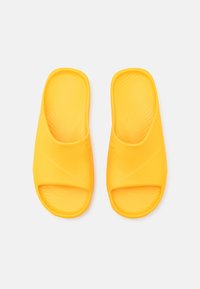 Chanclas amarillas de caucho suave, con punta abierta y plantilla texturizada, diseño curvado y un sutil detalle de marca.