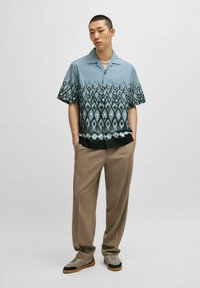 Camicia a maniche corte in blu sfumato, con motivo a diamante. Abbinata a pantaloni beige e sneaker grigie, su uno sfondo uniforme.