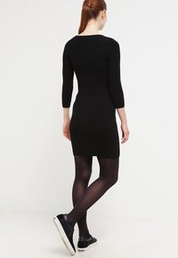 Svart ribbad klänning med trekvartslånga ärmar, figurnära silhuett och rundad halsringning, kombinerad med svarta strumpbyxor och sneakers.