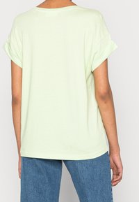 Jasnozielona koszulka z krótkim rękawem o luźnym kroju, okrągłym dekolcie i podwiniętych rękawach, wykonana z miękkiego materiału bawełnianego.
