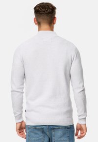 Suéter de punto gris claro con un acabado texturizado, mangas largas y cuello doblado, combinado con pantalones de mezclilla azules.