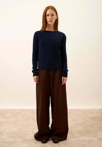 Granatowy sweter prążkowany z długimi rękawami, połączony z szerokimi brązowymi spodniami. Gładka tekstura, luźny krój, minimalistyczny styl, prosty okrągły dekolt.