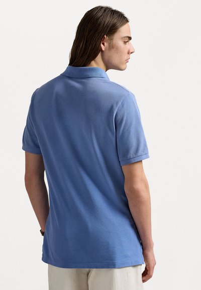 Light blue polo shirt with a collar, short sleeves, and textured fabric. Back view shows a relaxed fit and hem.