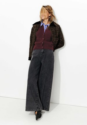 Veste léopard, cardigan bordeaux, chemise bleue, jeans gris à jambes larges, et talons noirs à clous. Fond minimal.