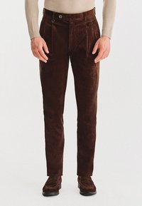 Brązowe spodnie w prążek o prostym kroju, z zaszewkami i zapięciem na guzik. Tkanina ma miękką, fakturowaną strukturę.