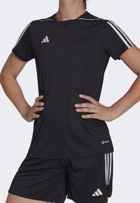 Camiseta deportiva negra de mangas cortas, con diseño de cuello en V, que presenta franjas blancas en los hombros y el logo de adidas en el pecho.