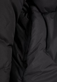 Interior de una chaqueta de acolchado negro con una textura suave y mate. Incluye un bolsillo interior y costuras cosidas para mayor calidez y estructura.