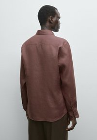 Braunes Leinenhemd mit spitzem Kragen, langen Ärmeln und abgerundetem Saum. Glatte Textur und Knopfdetails an den Bündchen.