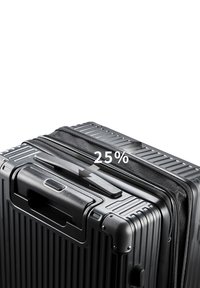 Maleta dura negra con textura acanalada horizontal, asa superior y cremallera; un gráfico muestra que se expande un 25%.