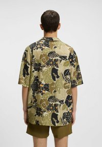 Korte mouwen overhemd met een multicolore botanische print met groene, zwarte en oranje accenten. Lichtgewicht stof, losse pasvorm, open kraag.