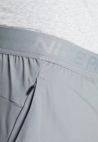 Grå atletiska shorts med en bred midja med präglad text "NIKE PRO", en dragkedjeficka och ett slätt, texturerat tyg.