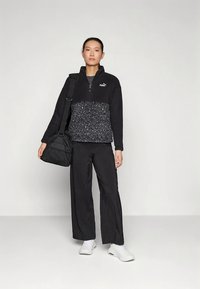 Czarny polarowy pulower z dolną częścią w panterkę, w połączeniu z czarnymi spodniami o szerokich nogawkach i białymi trampkami. Posiada zamek przy szyi i logo.