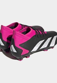 Mustat ja vaaleanpunaiset jalkapallokengät, joissa on teksturoitu pinta, valkoiset yksityiskohdat ja istuva muotoilu; sisältävät piikkejä pidon ja suorituskyvyn parantamiseksi.