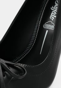 Crna kožna baletanka s detaljem mašne i natpisom "premium udobnost" na uložaku.