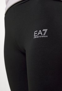 Leggings neri realizzati in un materiale liscio e stretchy. Presentano un logo EA7 Emporio Armani bianco sul lato.