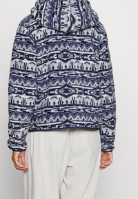 Sweatshirt con cappuccio in pile nei colori blu navy e azzurro con motivi geometrici. Caratterizzato da una vestibilità comoda, maniche lunghe e tessuto testurizzato.