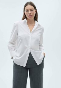 White button-up shirt with a collar and long sleeves, paired with charcoal gray pinstriped trousers, made from smooth, lightweight fabric.