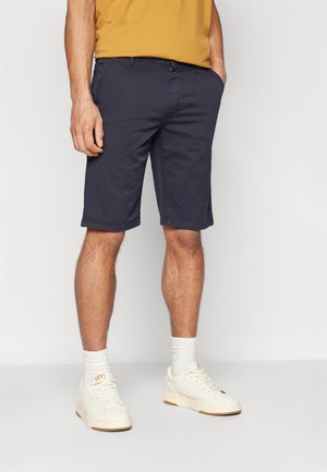 Pantalones cortos azul marino de mezcla de algodón, con un corte ajustado, dobladillos enrollados y bolsillos, combinados con zapatillas blancas y calcetas hasta el tobillo.