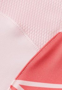 Rosa Stoff mit strukturiertem Mesh und glatten Abschnitten. Enthält einen lebhaften Korallenton mit weißen geometrischen Formen. Sichtbare genähte Kanten.