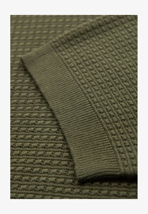 Tessuto di maglia verde textured con un polsino a coste. Presenta un motivo a griglia che crea profondità e variazioni di interesse visivo.