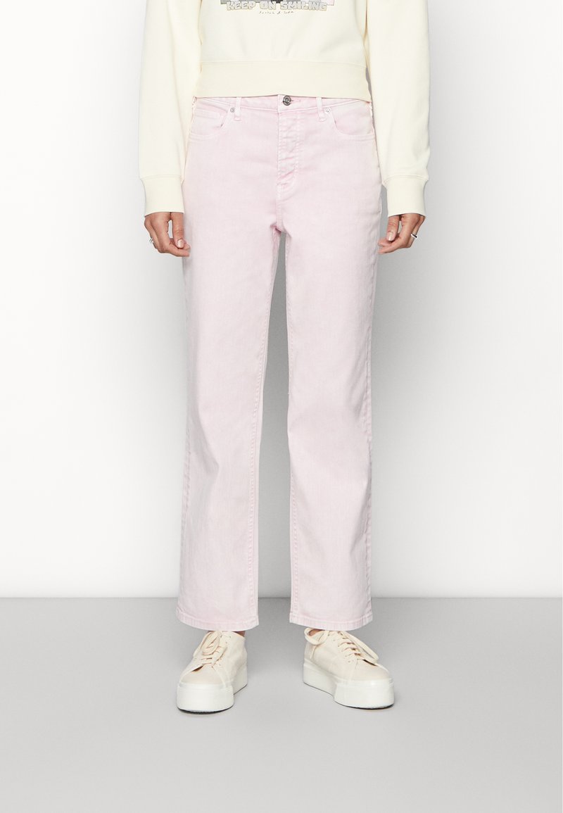 Jeans de ganga rosa claro com um design de perna reta, estilo de cinco bolsos e fecho de botão. Usados com um moletom de cor creme e ténis brancos.