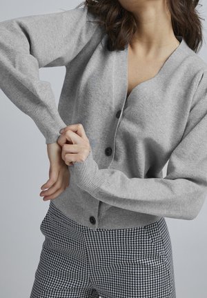 Grijze gebreide cardigan met een V-hals, vijf donkere knopen en geribbelde manchetten, gecombineerd met zwart-witte houndstooth patroonbroeken.