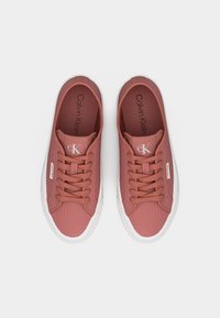 Paire de baskets à lacets Calvin Klein rose poudré avec tissu texturé et semelles en caoutchouc blanches, vues de dessus sur un fond blanc.