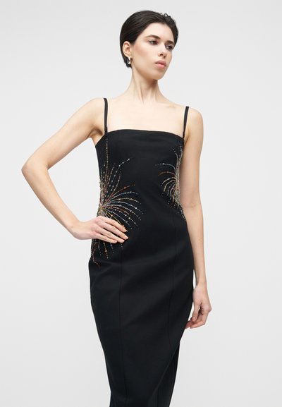 Fekete spagettipántos ruha, testhez simuló sziluettel. Gyöngy díszítések, amelyek tűzijátékra emlékeztetnek az oldalakon. Simává eső szövet textúra.