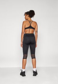 Reggiseno sportivo nero e leggings capri con pannelli in rete ai polpacci, caratterizzati da una texture liscia e un design aderente. Le scarpe da ginnastica completano il look.