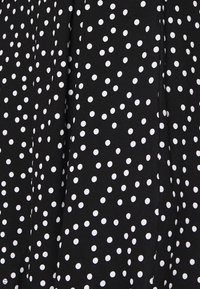 Tissu noir avec un motif de pois blancs, texture lisse et design drapé, adapté aux vêtements ou aux textiles.