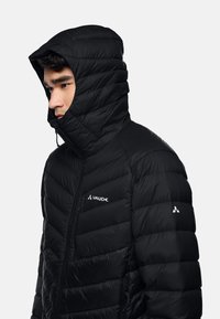Giubbotto piumino nero con colletto alto e cappuccio regolabile, caratterizzato da una design a coste cucito e logo sul petto sinistro e sulla manica.