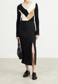 Sorte figursyet nederdel med sideslids, parret med en langærmet sweater med et geometrisk design i sort, hvid og beige. Sort taske og sko.