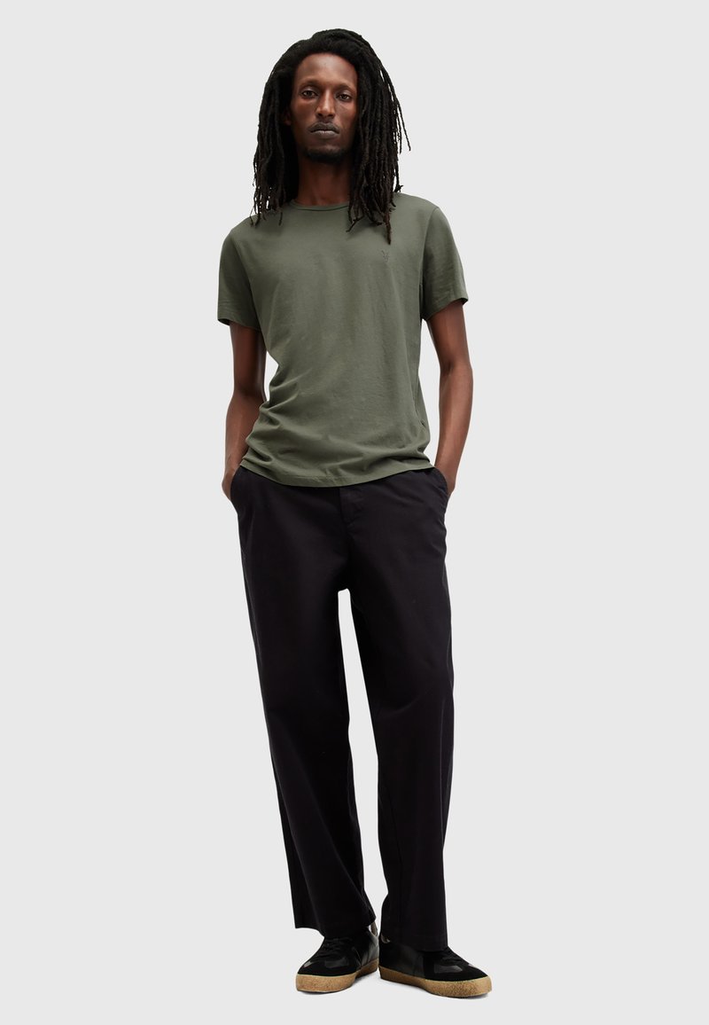 T-shirt in cotone verde oliva con scollatura rotonda, abbinata a pantaloni neri larghi e sneaker nere con suola color marrone chiaro.