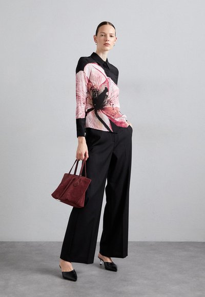 Blusa nera a fiori con motivo rosa, maniche lunghe e colletto, abbinata a pantaloni neri a vita alta e una borsa in suede bordeaux.
