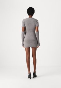 Robe grise en maille avec manches courtes et poignets étendus, coupe ajustée, tissu texturé, associée à des chaussures à talons noirs.