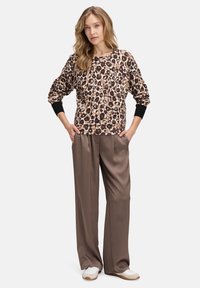Bluza w panterkę z długimi rękawami, czarnymi mankietami i luźnymi brązowymi satynowymi spodniami, noszona z białymi sneakersami. Casualowy projekt stroju.