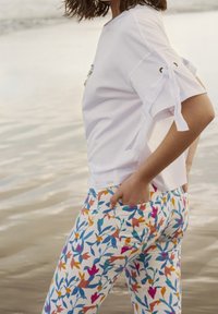 Bílé tričko s krátkým rukávem a bočními uzly, spárované s barevnými květinovými kalhotami s modrými, oranžovými a růžovými květinami na bílém pozadí.