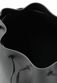 Bolso de cuero negro en forma de cubo con un borde superior ondulado, que cuenta con correas de cordón negras y una textura interior suave. Sin hardware o patrones visibles.