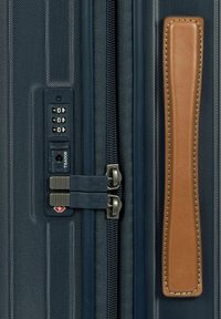 Valigia rigida navy con esterno testurizzato, doppie cerniere in metallo, lucchetto a combinazione TSA e un manico in pelle marrone come accentuazione.