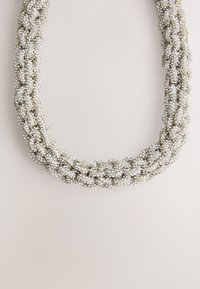 Braided necklace featuring silver beads with a textured surface, arranged in a twisted design. Color is predominantly silver with light accents.