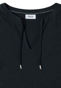 T-shirt noir à col rond avec une encoche en forme de V et des lacets, avec une étiquette blanche portant le texte "CECIL" à l'intérieur du col.