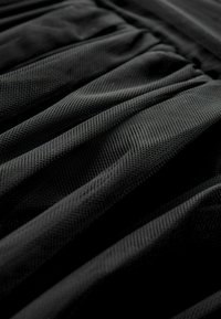 Černá texturovaná tkanina s plisovaným designem, vykazující jednotný vzor a jemný vzhled. Důraz na vrstvy a záhyby v materiálu.