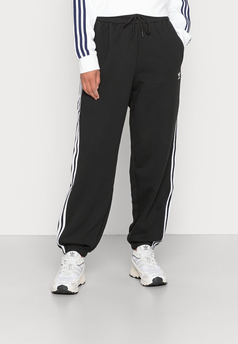 Svarta sweatpants med vita sidostråken, elastisk midja och muddar. Tillverkade av mjukt tyg, med en logotyp från varumärket på framsidan.