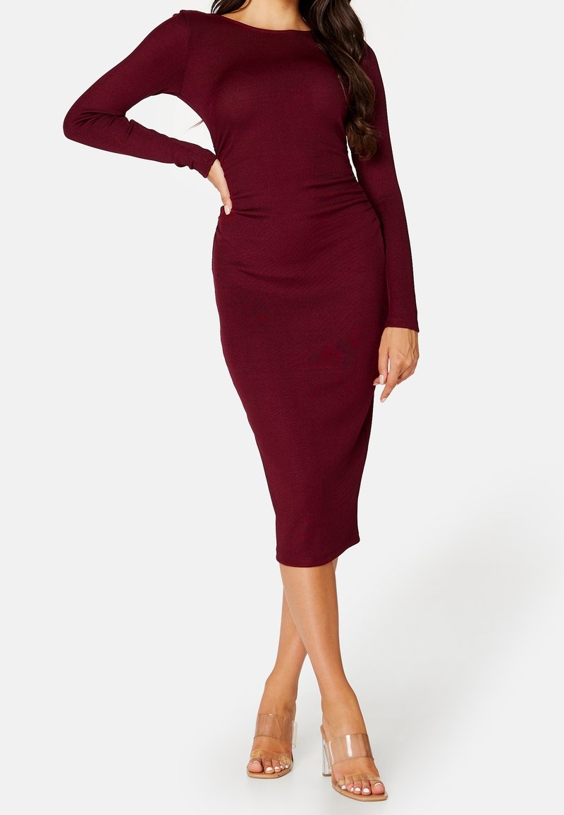 Bordeaux långärmad bodycon-klänning med båthals, ribbad struktur och knälång design, matchad med genomskinliga stilettklackar.