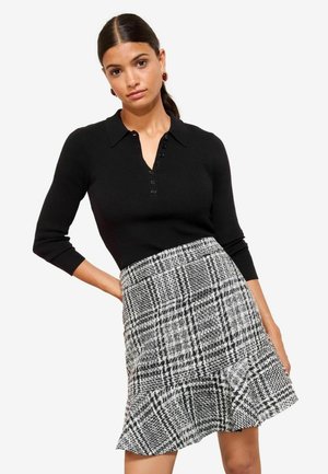 Black ribbed knit top with a collared neckline and button details, paired with a black and white patterned skirt featuring a flared hem.