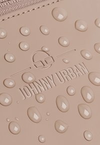 Materiale impermeabile beige con gocce in rilievo sulla superficie; logo in rilievo "JOHNNY URBAN" in un carattere moderno. Dettagli del design testurizzati.