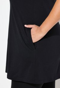 Svart tunika i mjukt tyg, med sidficka, rundad nederkant och avslappnad passform. Slät textur med minimala sömmar.