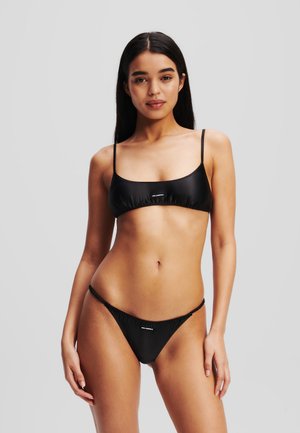 Conjunto de bikini negro con tirantes finos. La parte superior tiene un escote cuadrado, mientras que la parte inferior es de corte bajo con detalles fruncidos en los laterales. Textura suave.