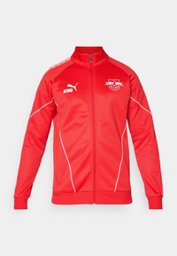 Red athletic jacket with a high collar, full zip, and white accents. Features logos on the chest and shoulder. Made from smooth fabric.